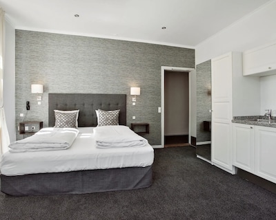 Dobbeltværelse med grå væg, seng, natborde og tekøkken i Sanders Park lejlighed.