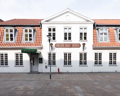 Go Hotel Herlev med hvid facade, rødt tegltag og "Herløv Kro" skilt.