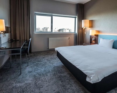 Hotelværelse med dobbeltseng, skrivebord, vindue og byudsigt.