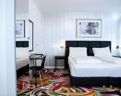 Moderne hotelværelse med dobbeltseng, skrivebord og farverigt tæppe på gulvet.